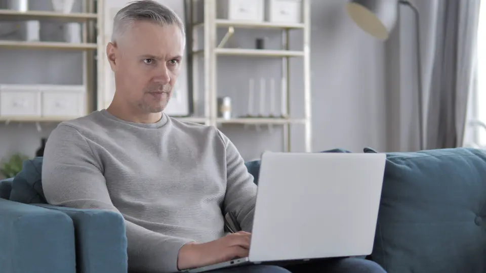 A grey-haired man on a video call at his laptop