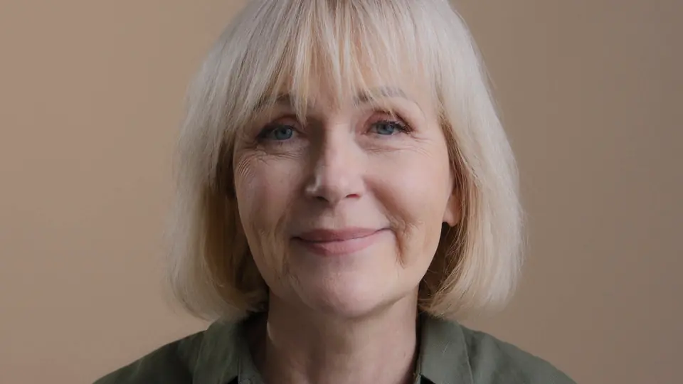 A grey-haired woman smiling, mid-conversation